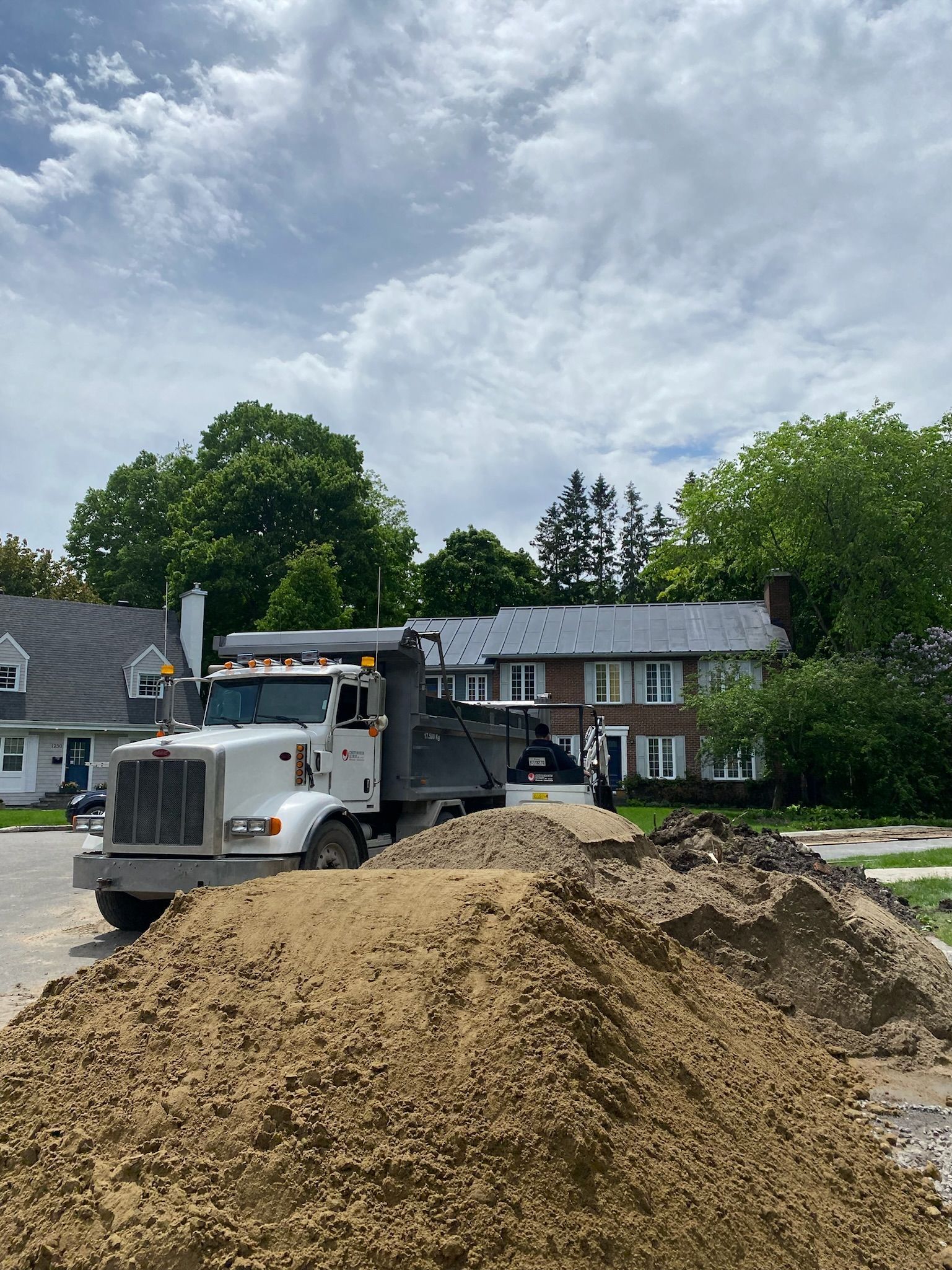 Un camion à benne basculante roule dans une rue à côté d'un tas de terre.