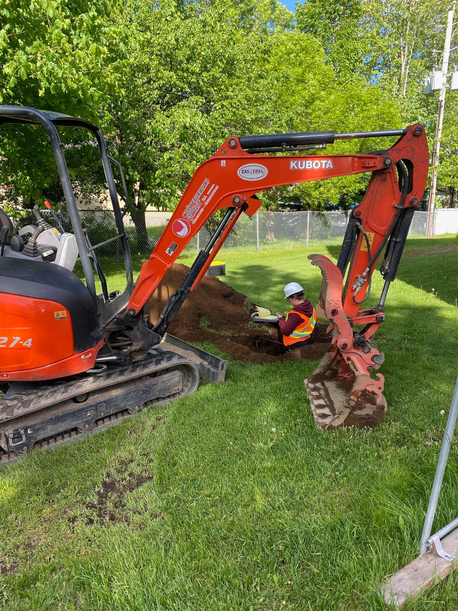 Une excavatrice creuse un trou dans l'herbe d'une cour.
