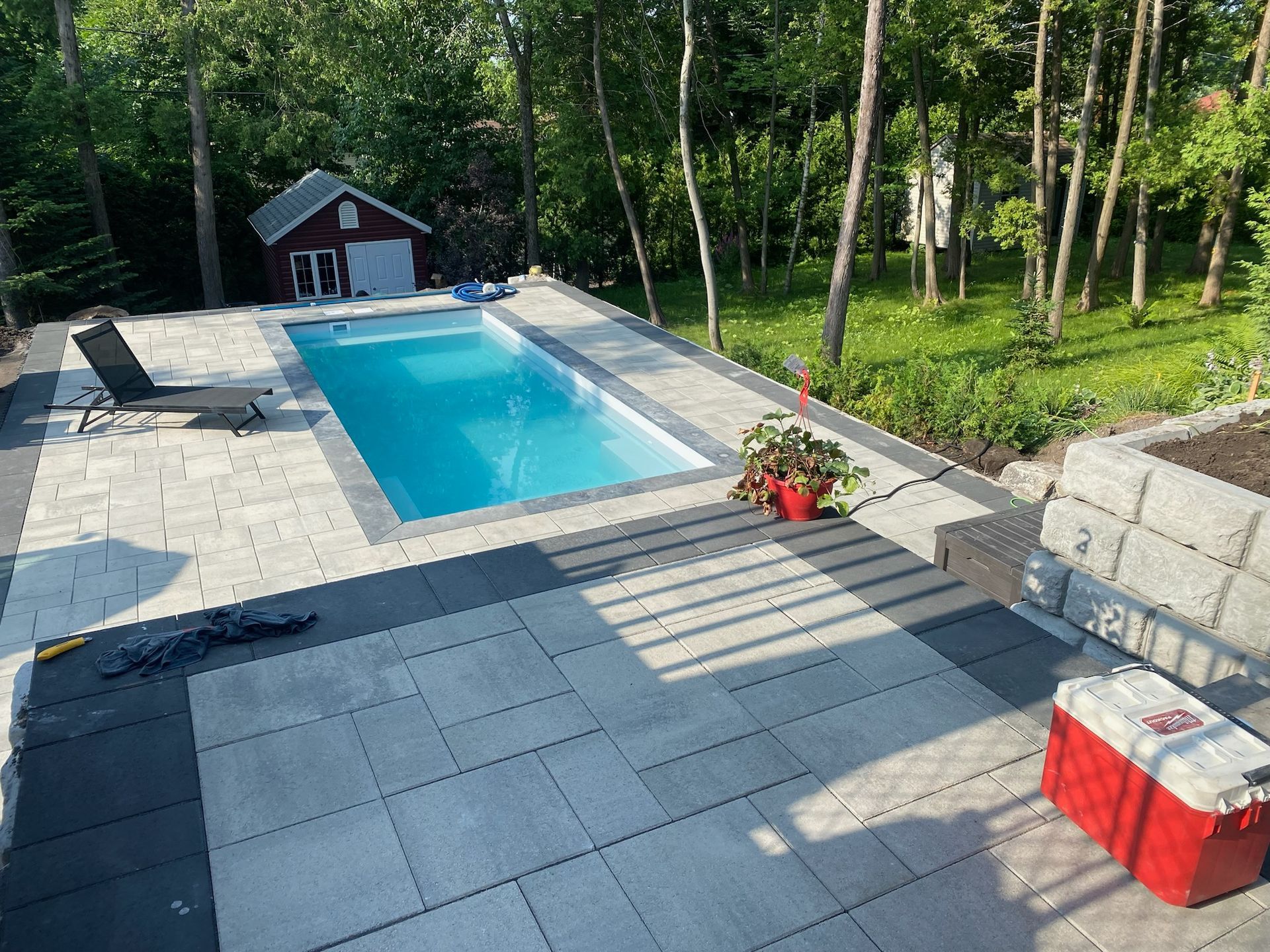 Une grande piscine est entourée d'un patio et d'une glacière rouge.