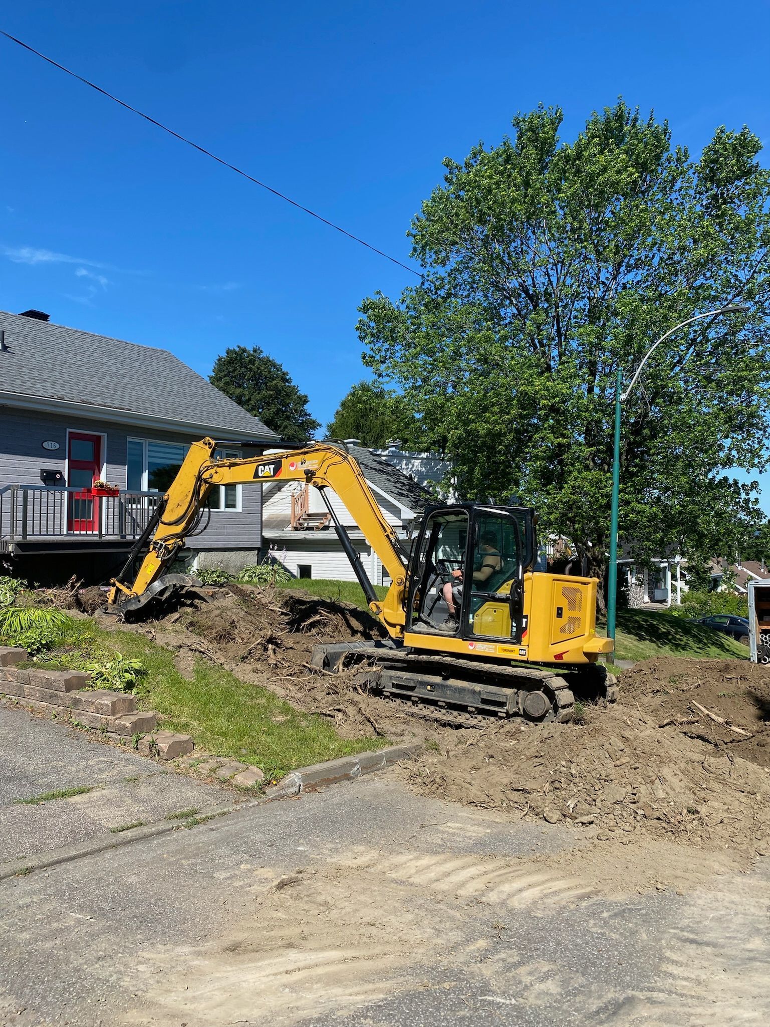Une excavatrice jaune creuse un trou devant une maison.