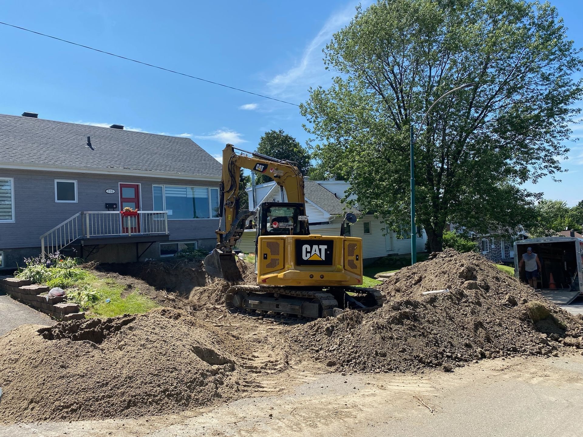 Une excavatrice à chat creuse un trou devant une maison.