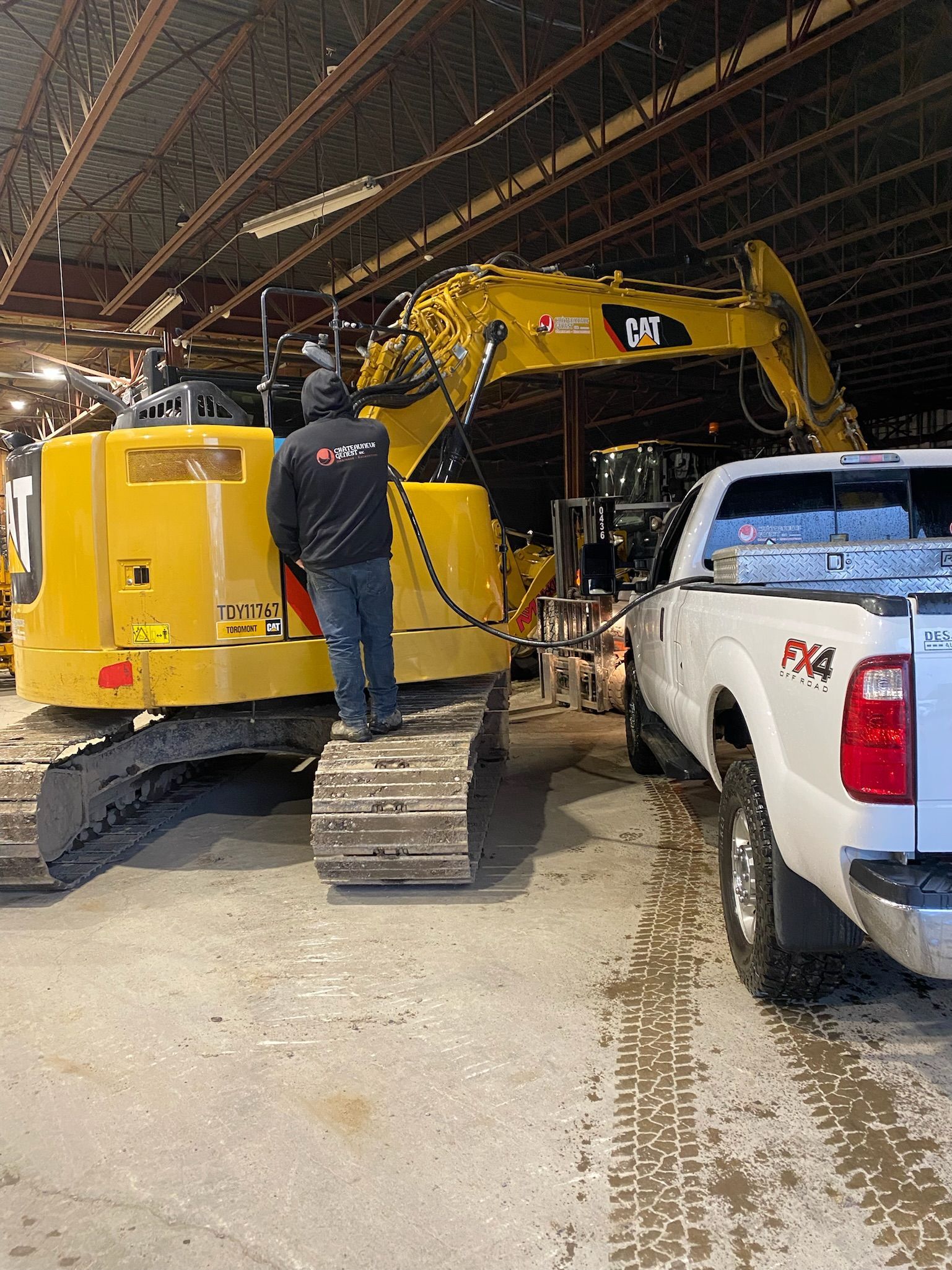 Un homme se tient debout sur une excavatrice jaune à côté d'un camion blanc.