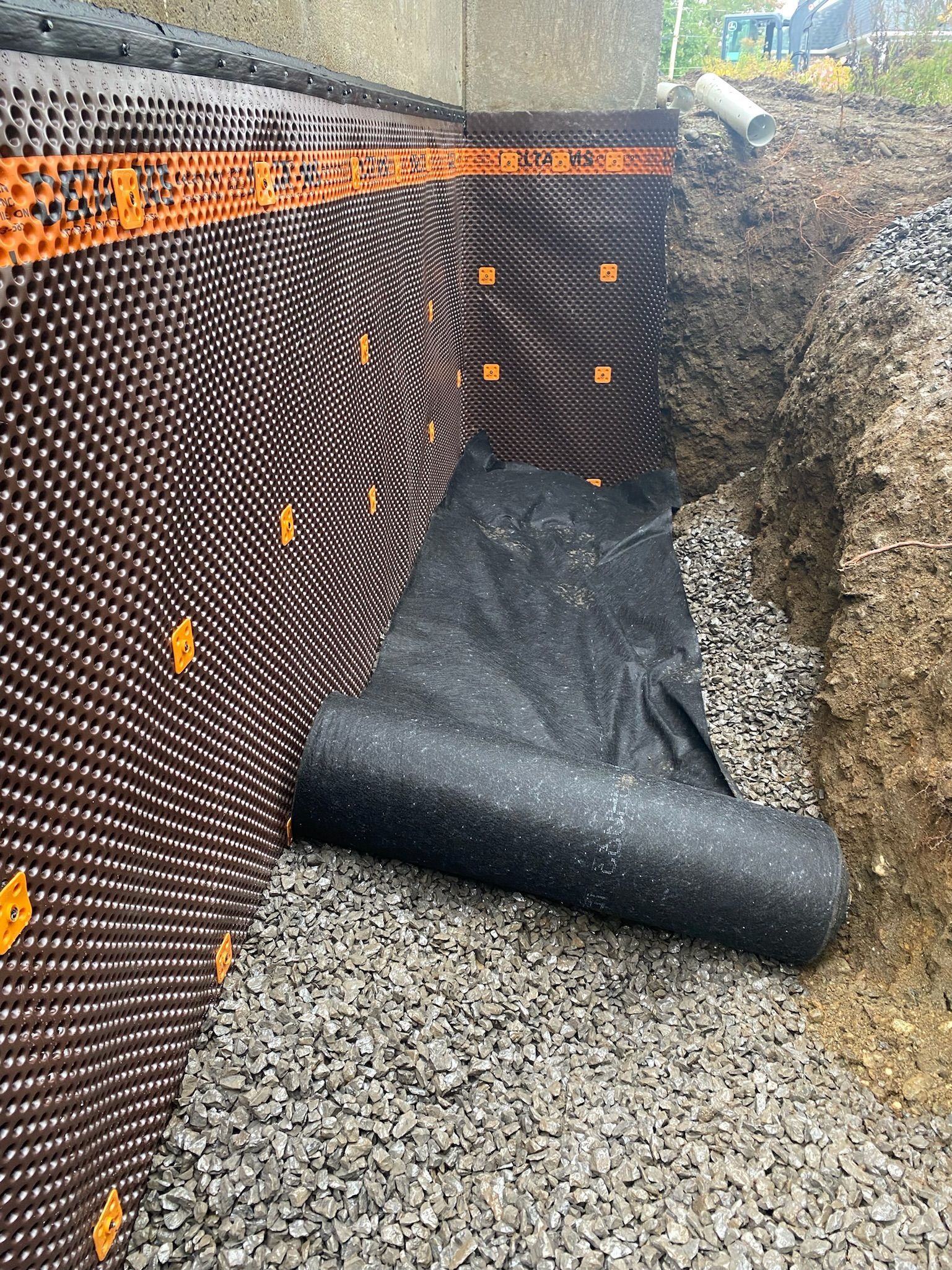 Un rouleau de membrane de drainage est placé dans un trou dans le sol.