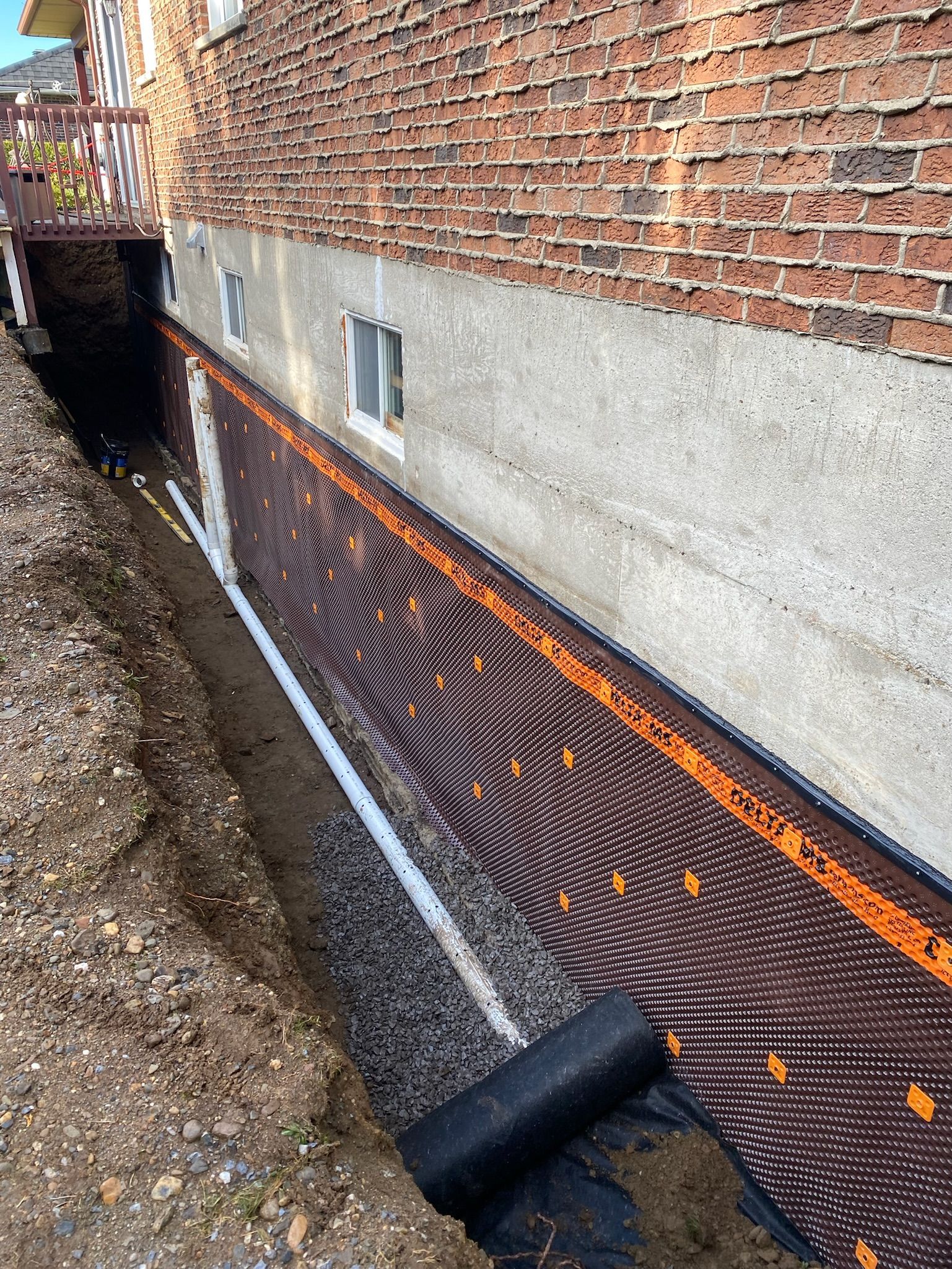 Un système de drainage est en cours d'installation sur le côté d'un bâtiment en briques.