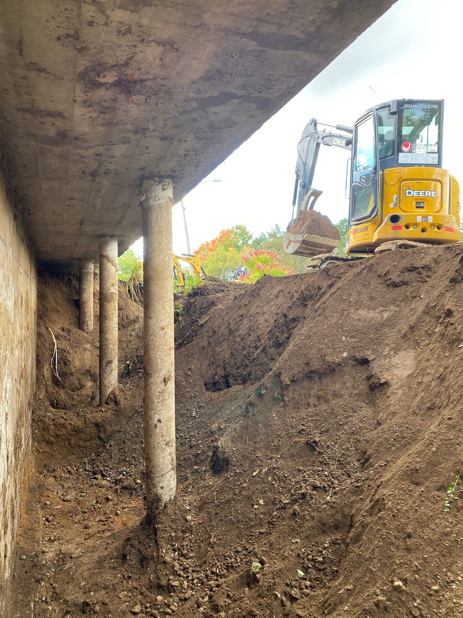 Une excavatrice jaune est assise sur un tas de terre sous un pont.