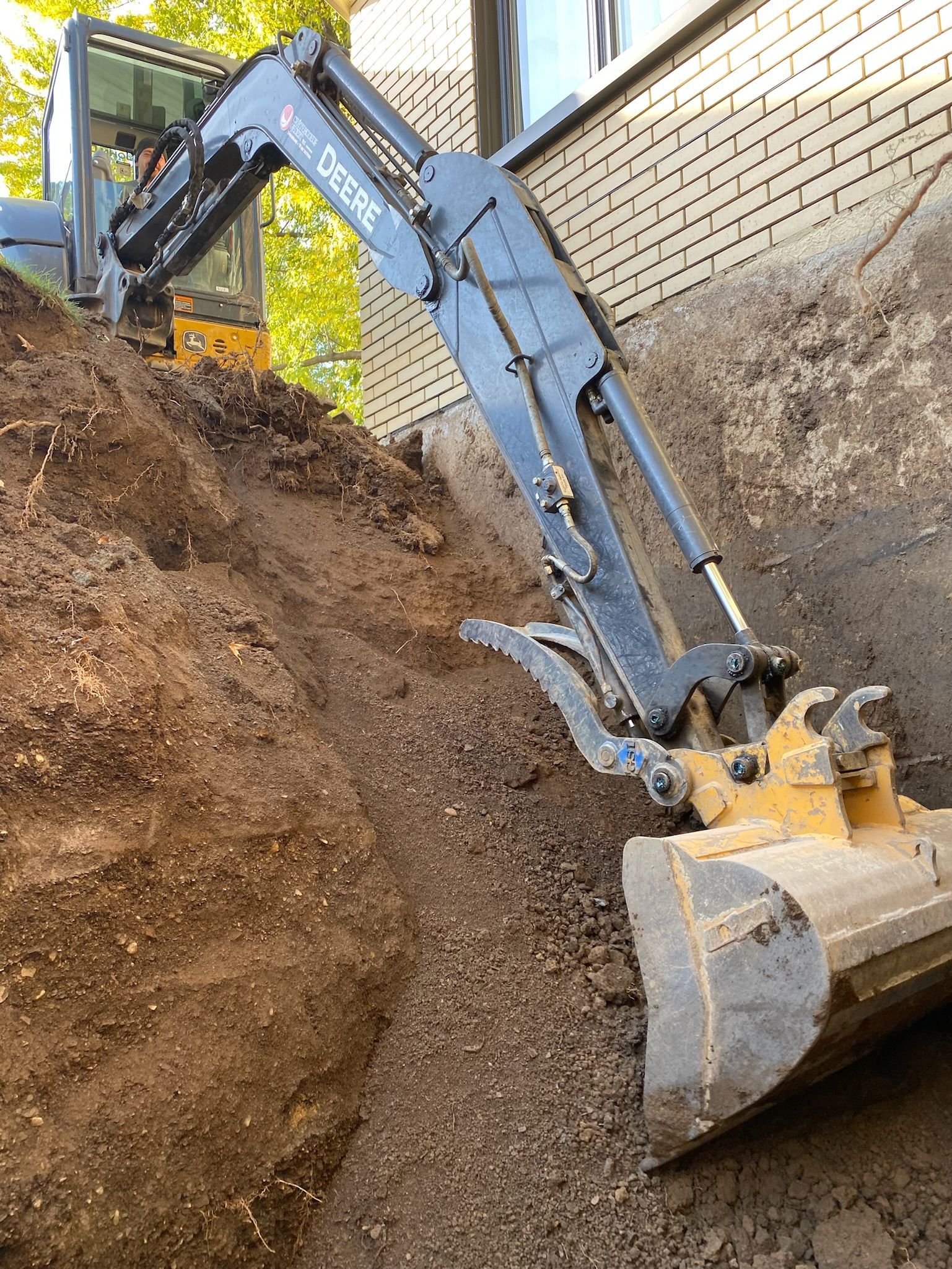 Un bulldozer creuse un trou dans le sol à côté d'un mur de briques.