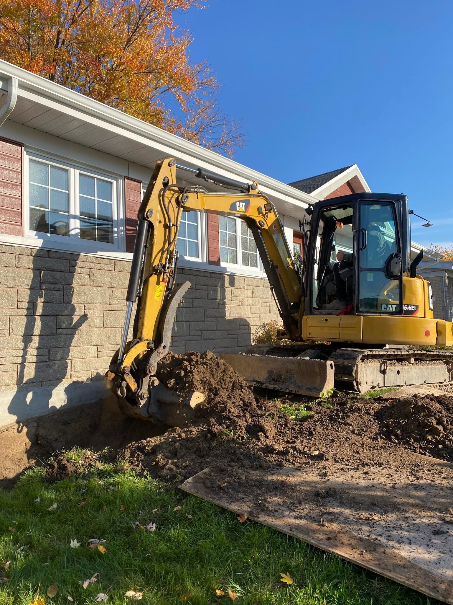 Une excavatrice jaune creuse un trou devant une maison.