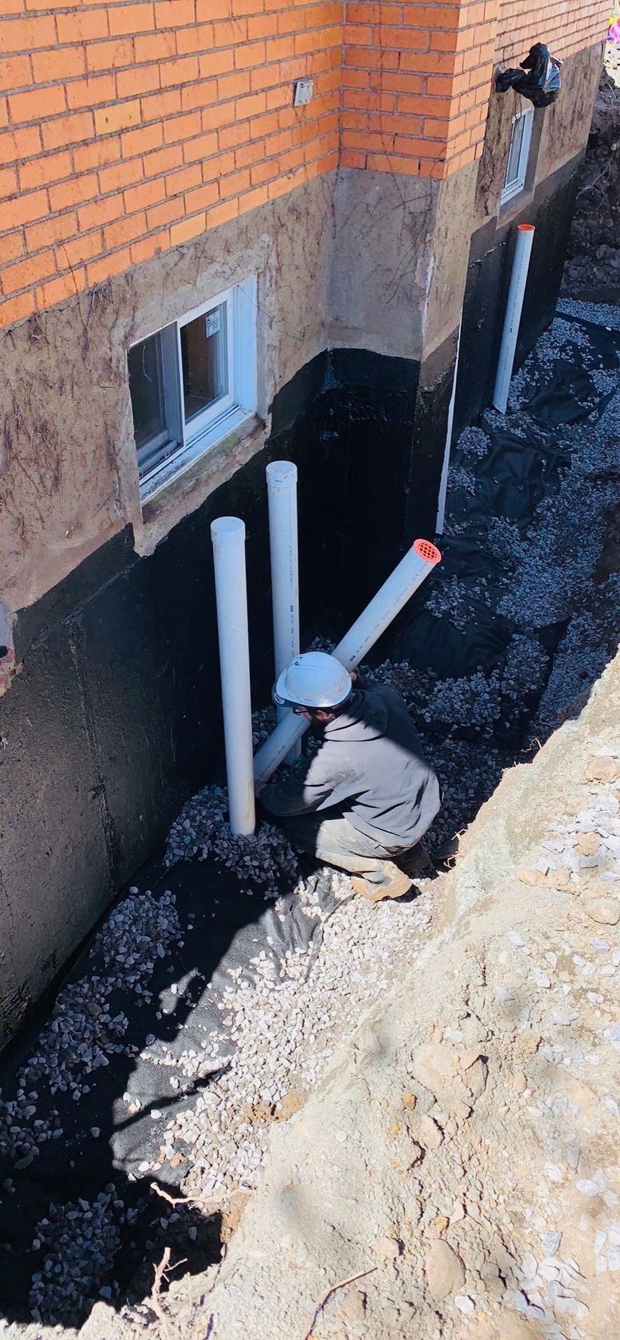 Un système de drainage est en cours d'installation sur le côté d'un bâtiment en briques.