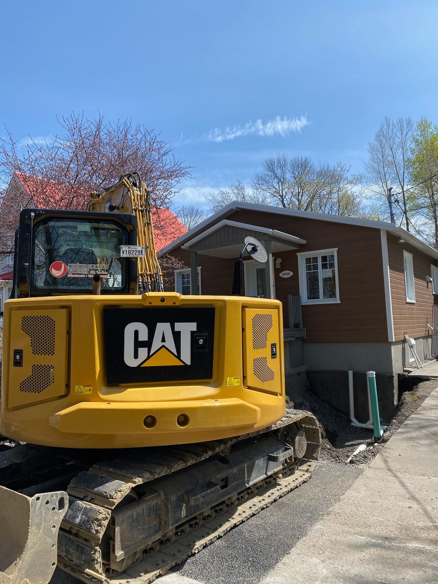 Une excavatrice jaune est garée devant une maison en briques.