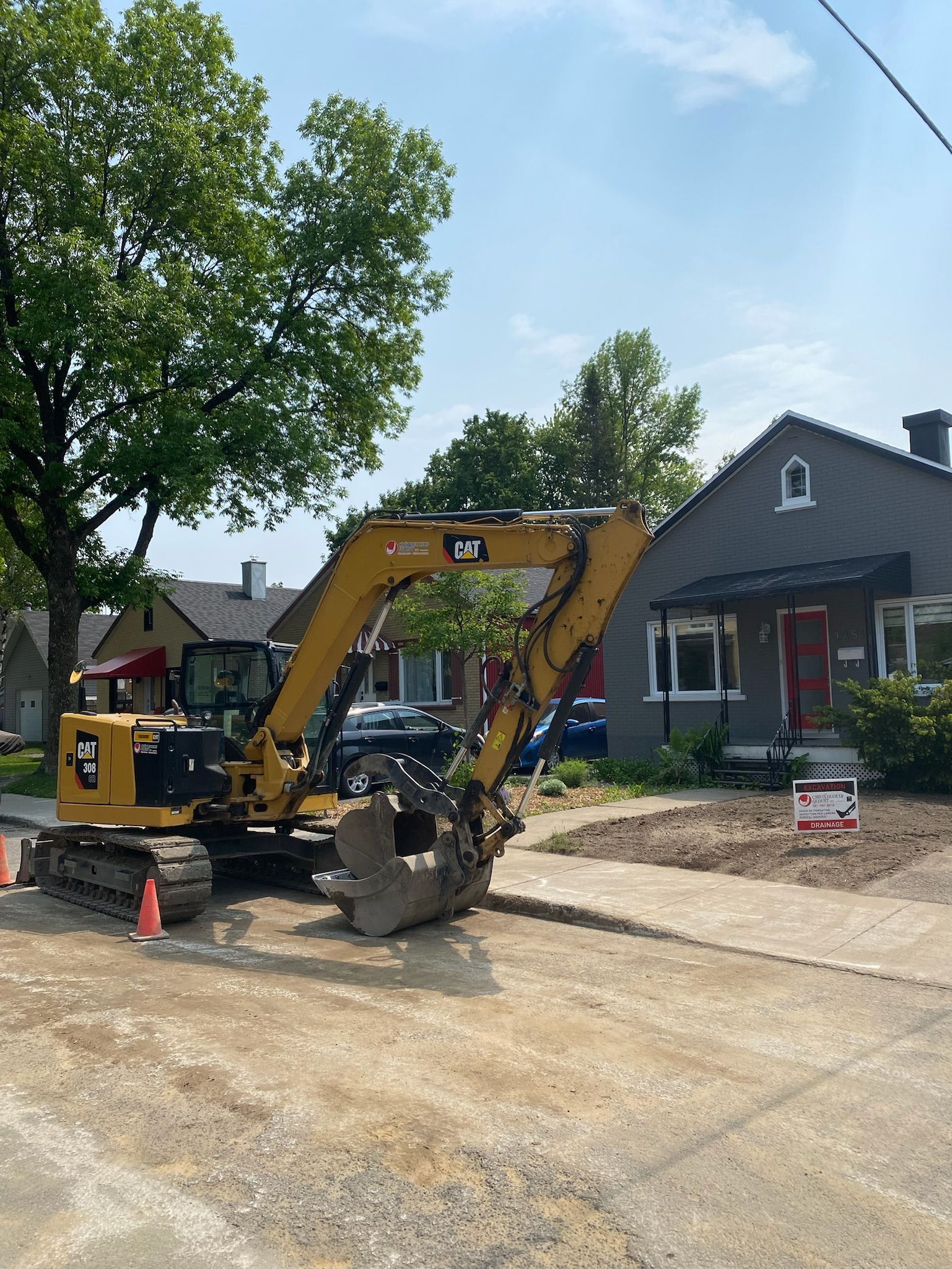 Une excavatrice jaune est garée sur le bord de la route devant une maison.