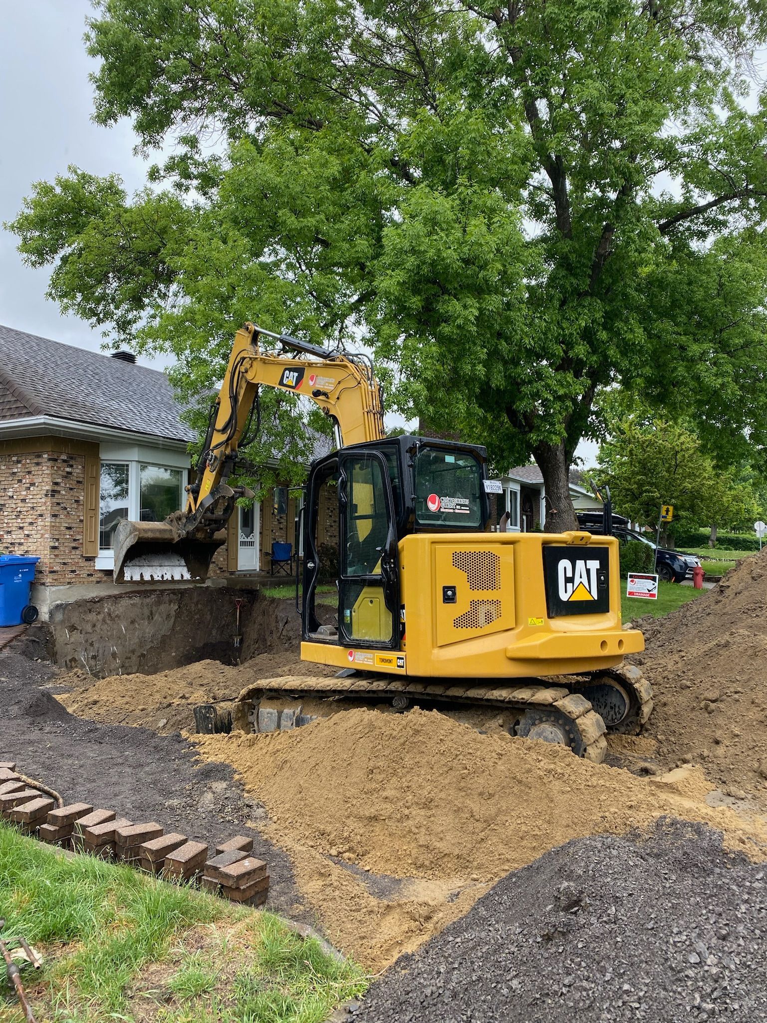 Une excavatrice jaune creuse un trou devant une maison.