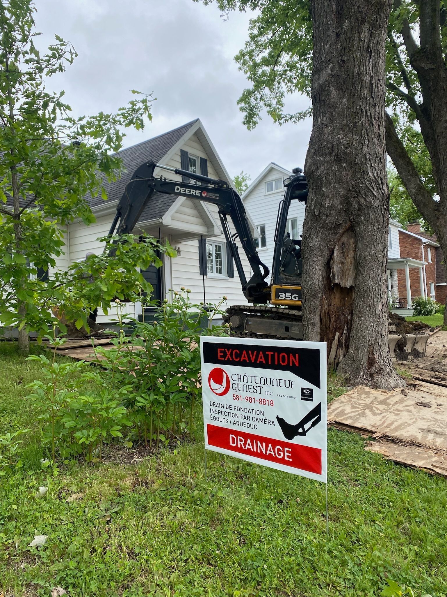Un panneau de construction est placé à côté d'un arbre devant une maison.