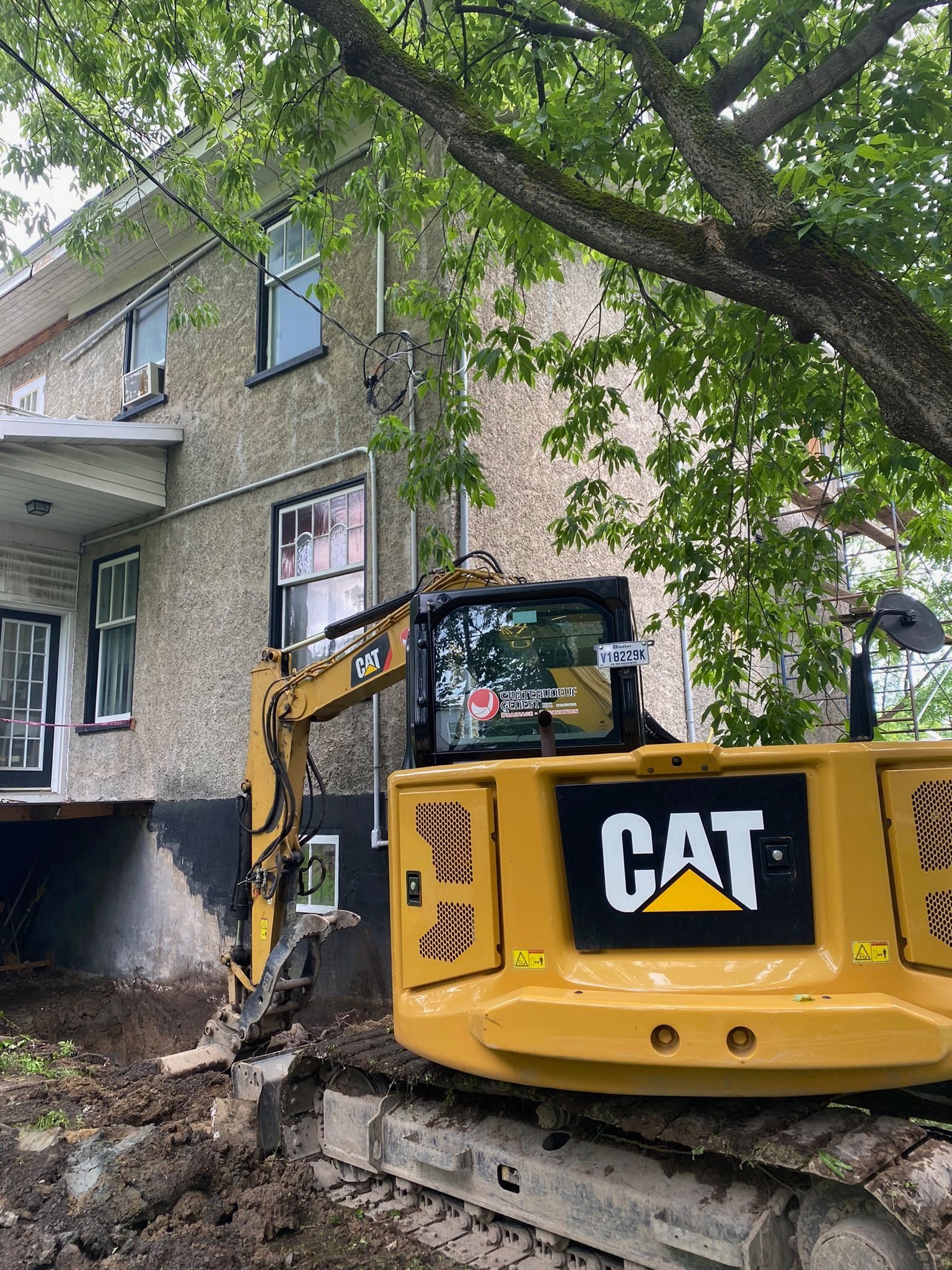 Une excavatrice jaune est assise devant une maison.