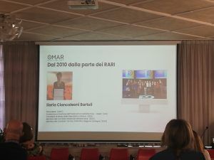 Schermata di presentazione con testo e foto; pubblico in primo piano.