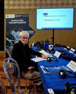 Donna seduta a un tavolo, con un monitor che mostra i dettagli del Wi-Fi. Sullo sfondo dell'evento è scritto 