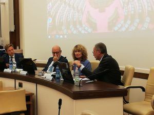 Quattro persone sedute a un tavolo da conferenza stanno parlando. Dietro di loro c'è uno schermo per le presentazioni.