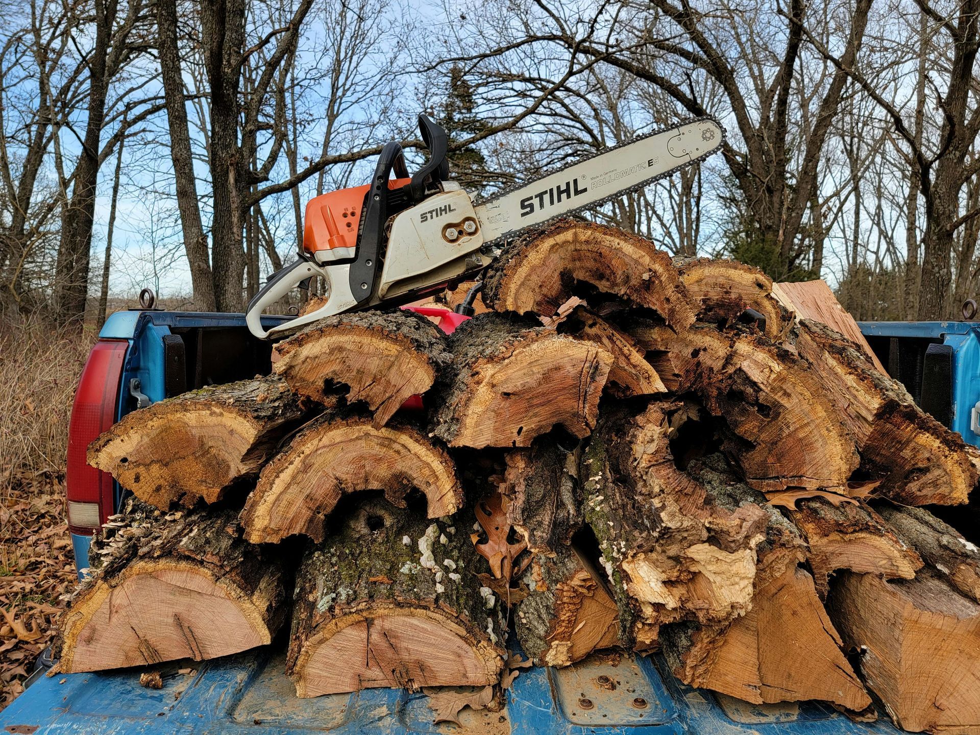 Pile of cut firewood in a truck bed with a chainsaw resting on top.