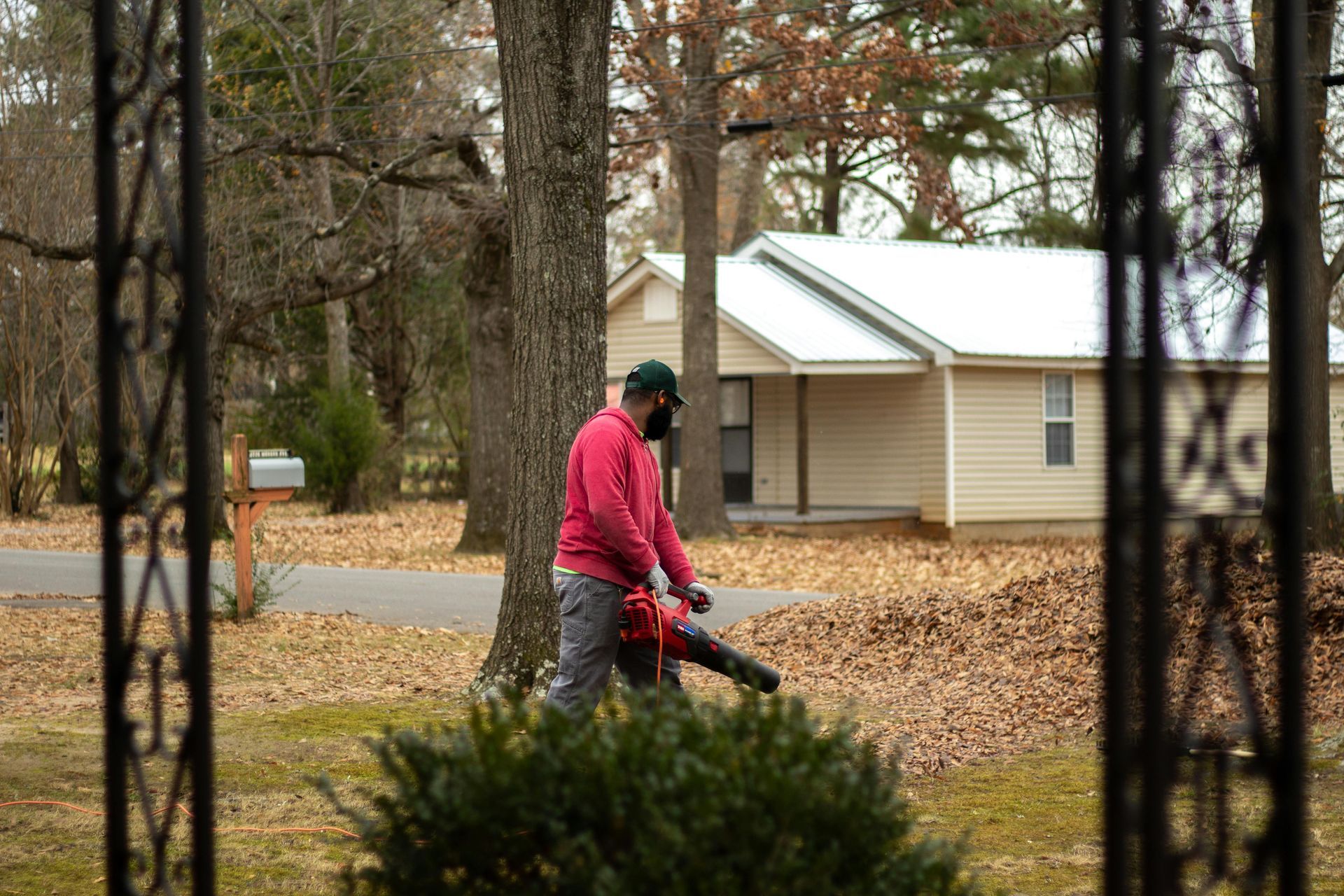 Man in red jacket and mask blowing leaves in front yard. Beige house in background.