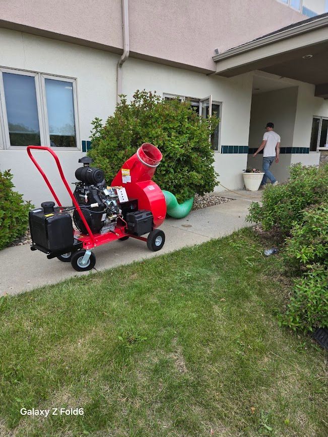 Red wood chipper on a paved path, near a building and bushes; a person walks nearby.