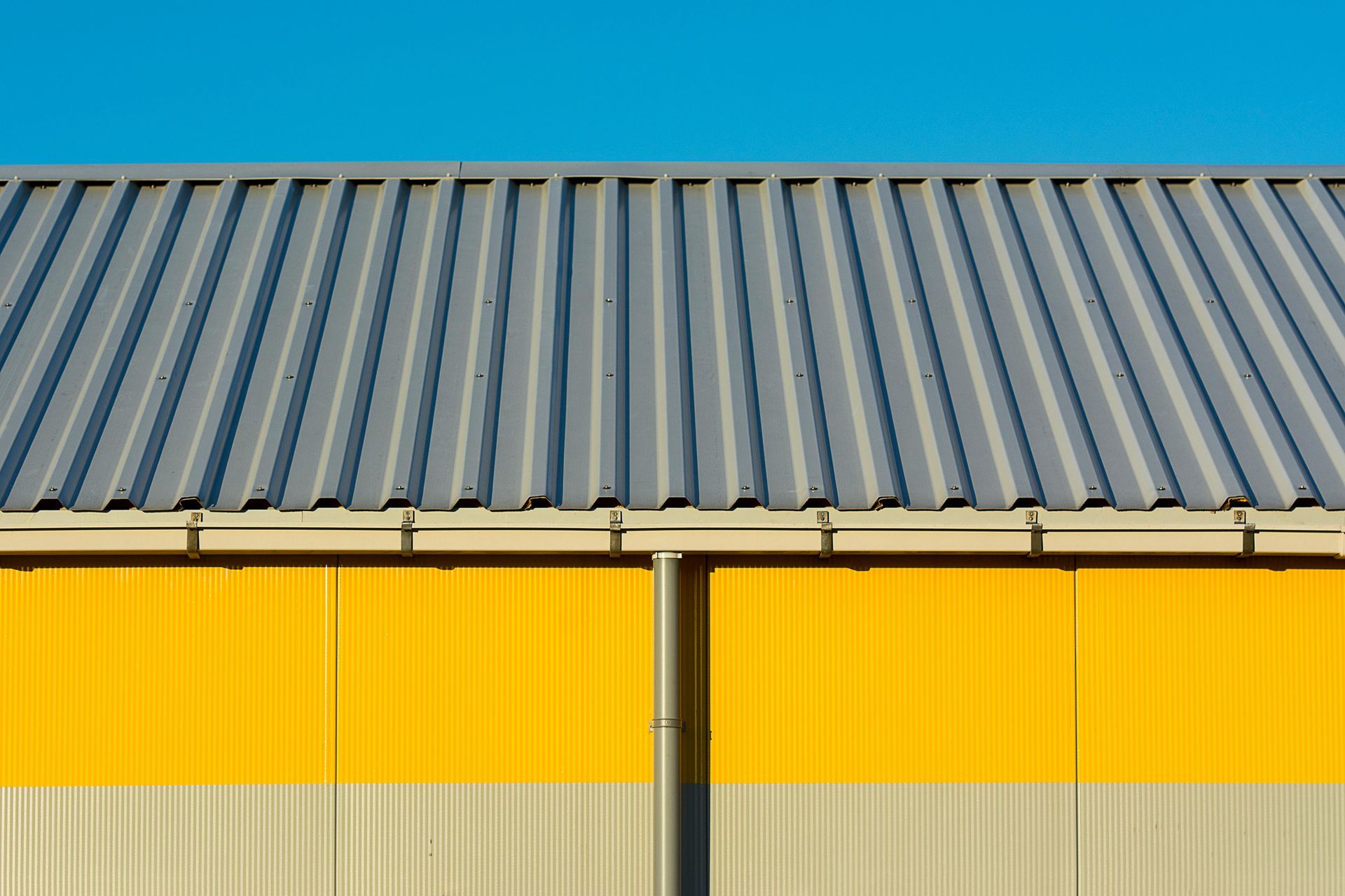 Grey corrugated metal roof over yellow and gray panels against a blue sky.