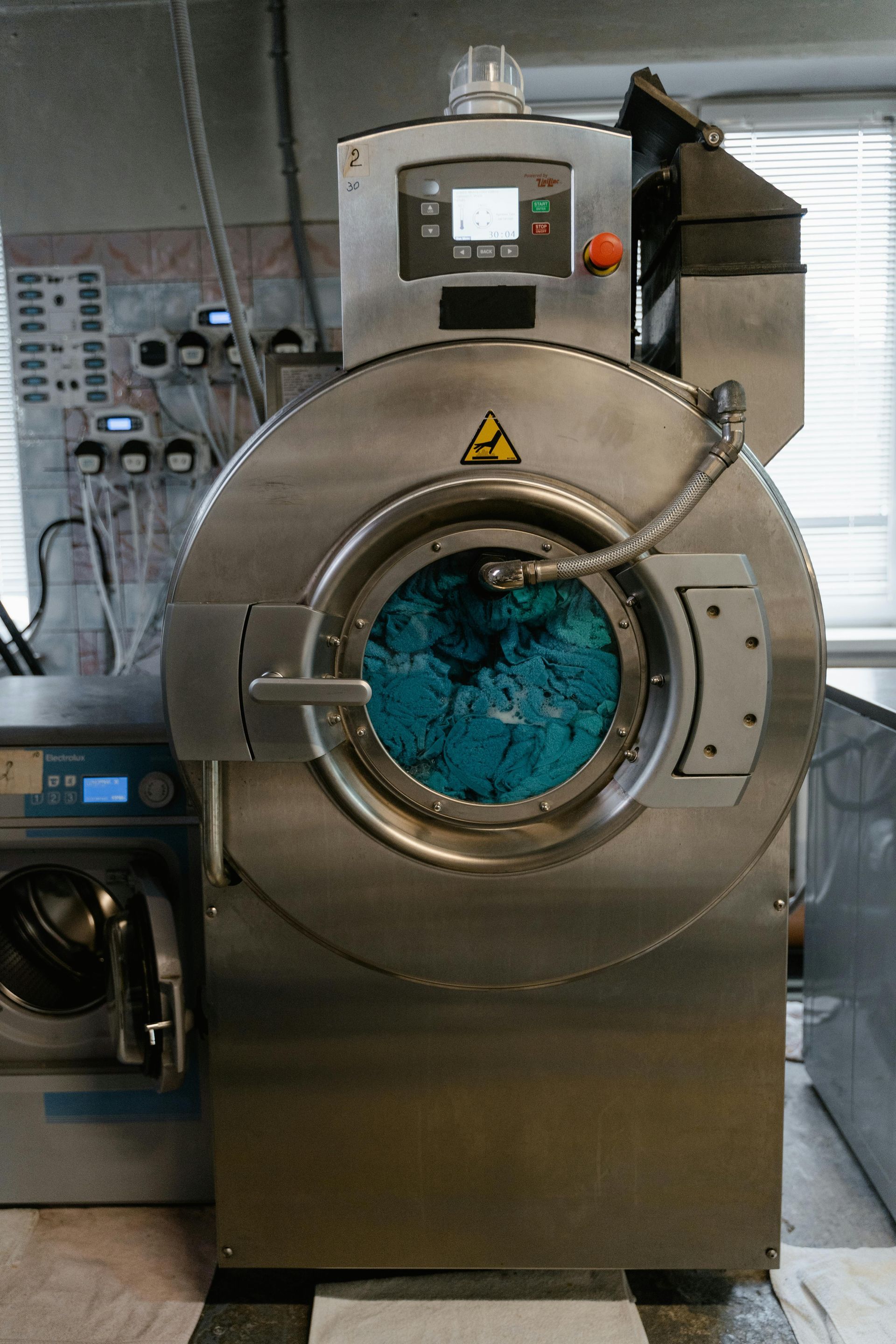 Industrial washing machine with a blue load, stainless steel finish.