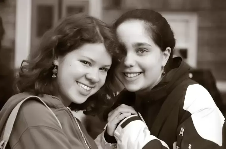 Two smiling people holding hands, outdoors. Sepia tone.