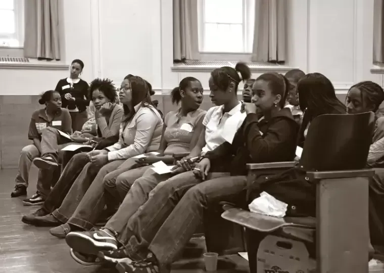People seated in a classroom listening to a presentation. A person stands behind them.