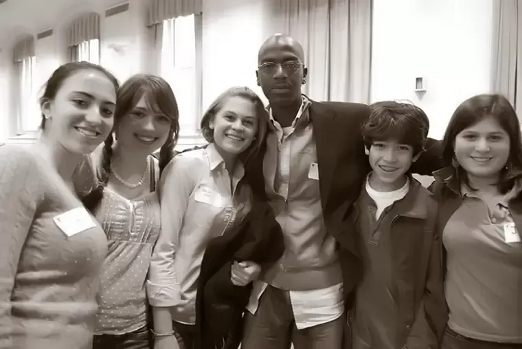 Group of six people smiling at the camera in a brightly lit room.