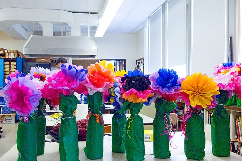 Colorful paper flowers in bottles wrapped with green paper on a table.