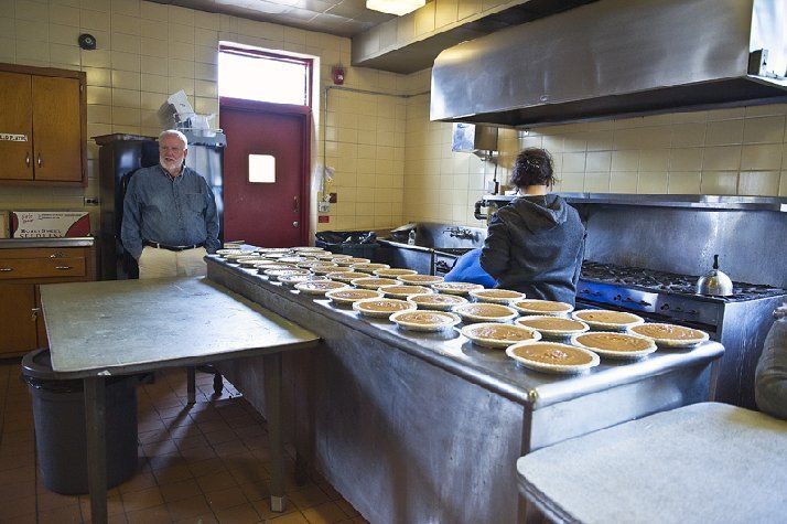 Two people in a commercial kitchen preparing pies on a long stainless steel counter.