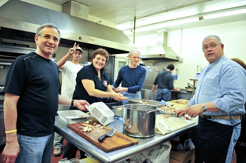 People preparing food in a commercial kitchen. Smiling, working around a stainless steel table