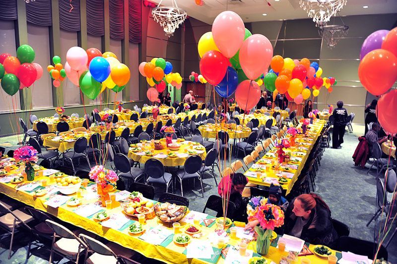 Party hall with colorful balloons, decorated tables, and people seated.