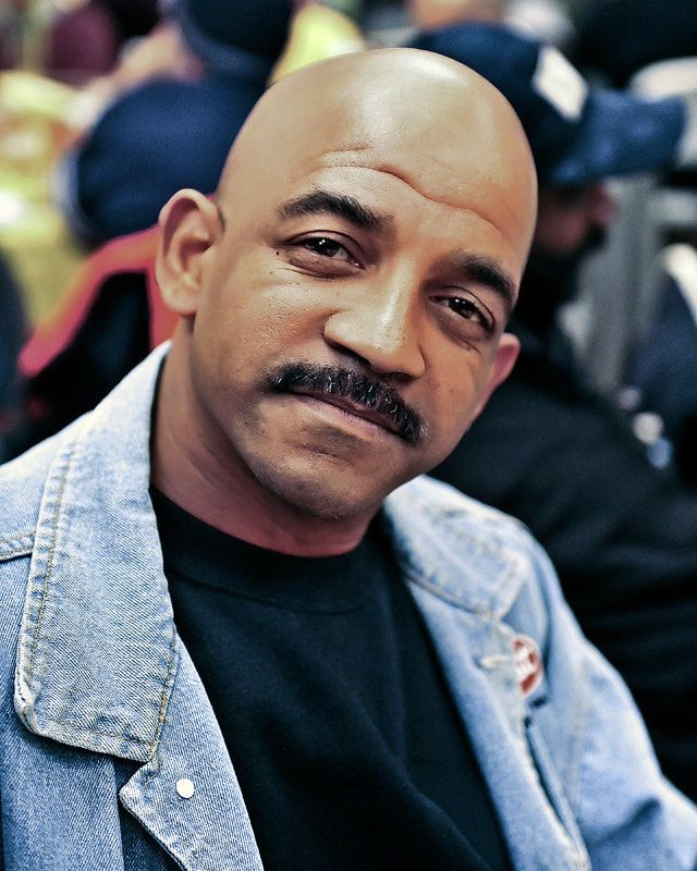 Bald man with mustache in denim jacket, looking at camera.