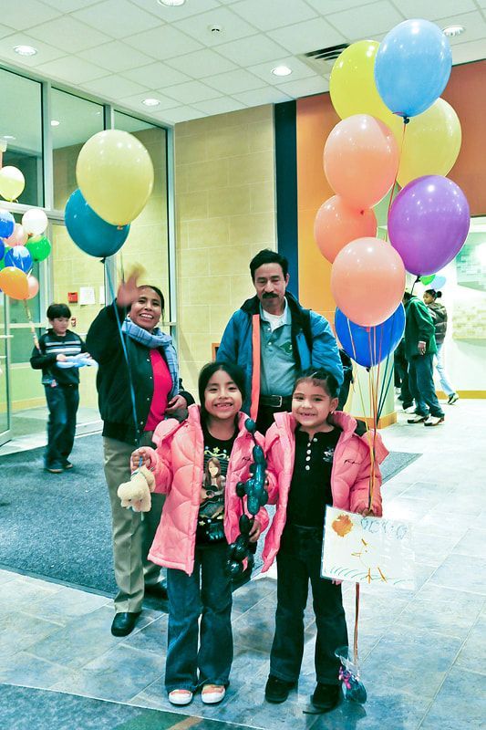 Family with balloons smiles and waves in a building lobby.