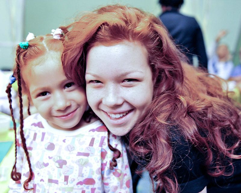 Two people with red hair smile, one child, one adult, close together.