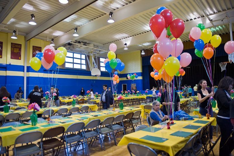 Large room decorated with balloons and tables set for an event; people are in attendance.
