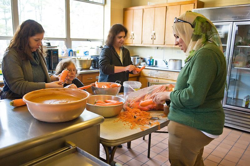 People peeling carrots in a kitchen. Sunlight streams in.