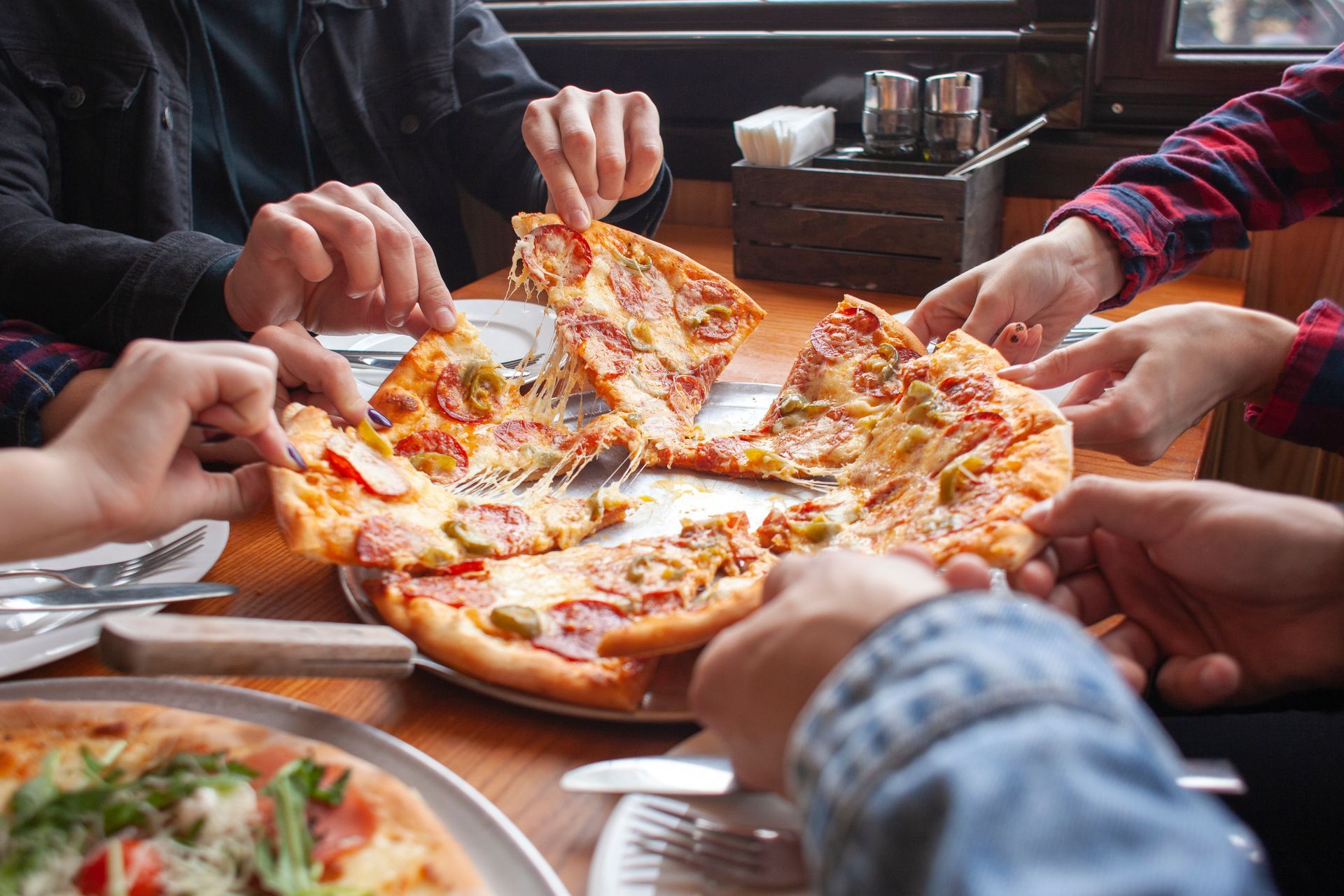 Group of people sharing a freshly baked pizza at a wooden table in an Italian restaurant.