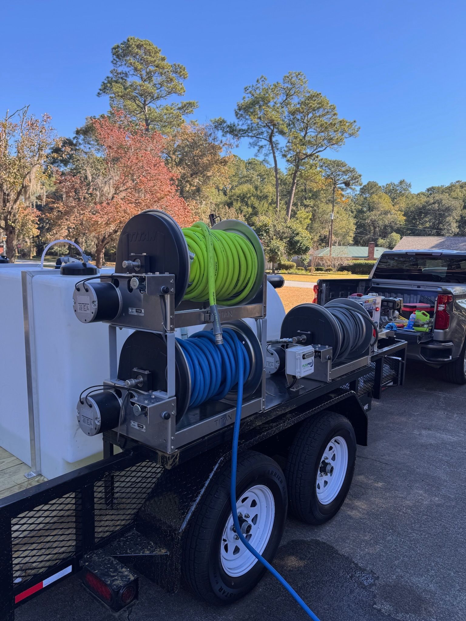 Trailer with tanks and reels of hose. Green, blue, and black hoses. Bright day.