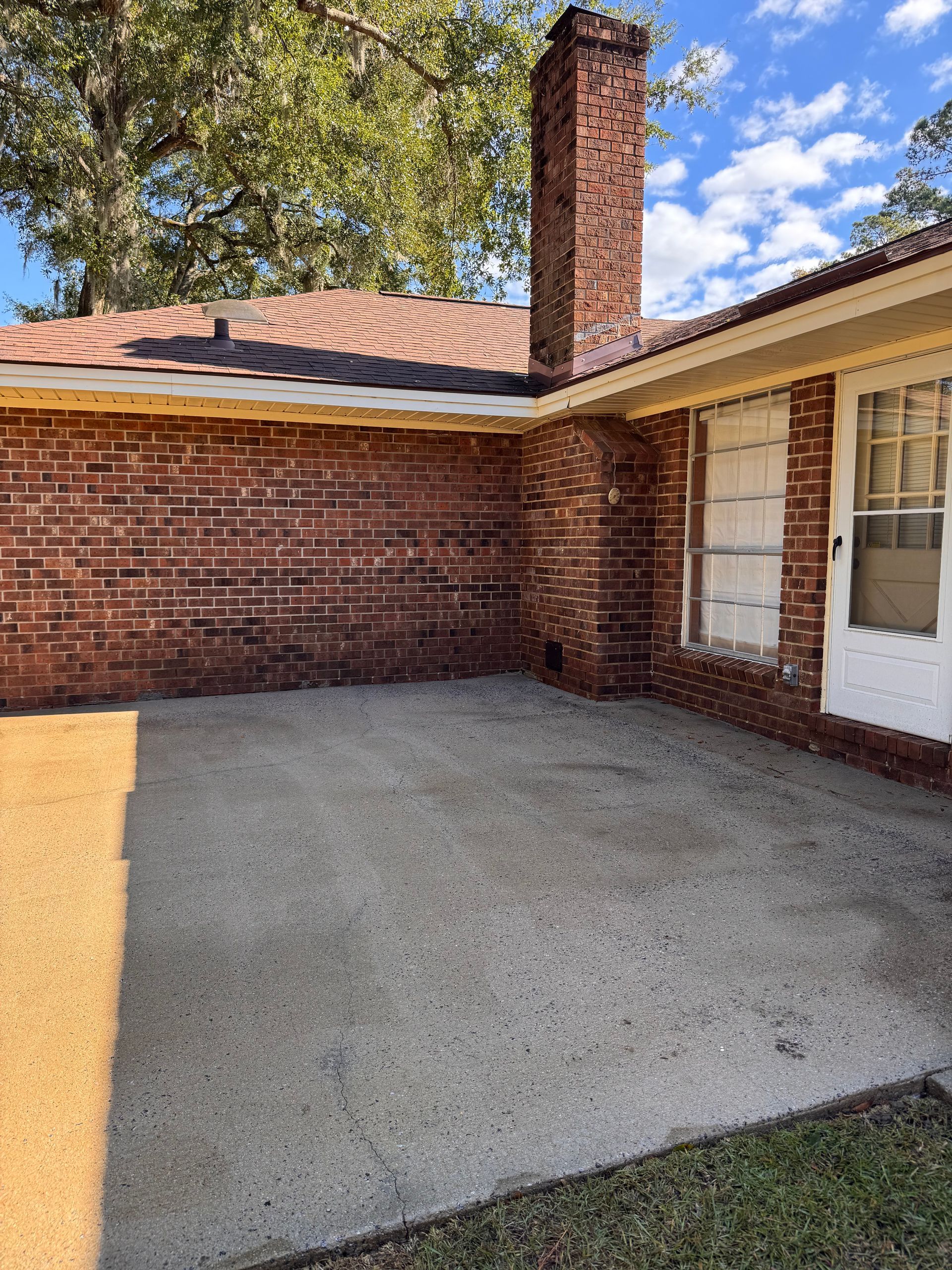Concrete patio beside a brick house with a chimney and a white door.