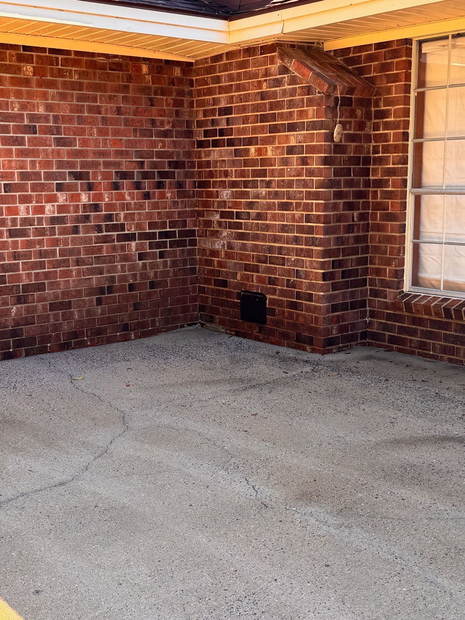 Corner of a brick building with a concrete floor. The bricks are dark red and the floor is gray.