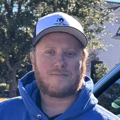 Owner Robbie Coggins in blue hoodie and hat stands beside a car with 