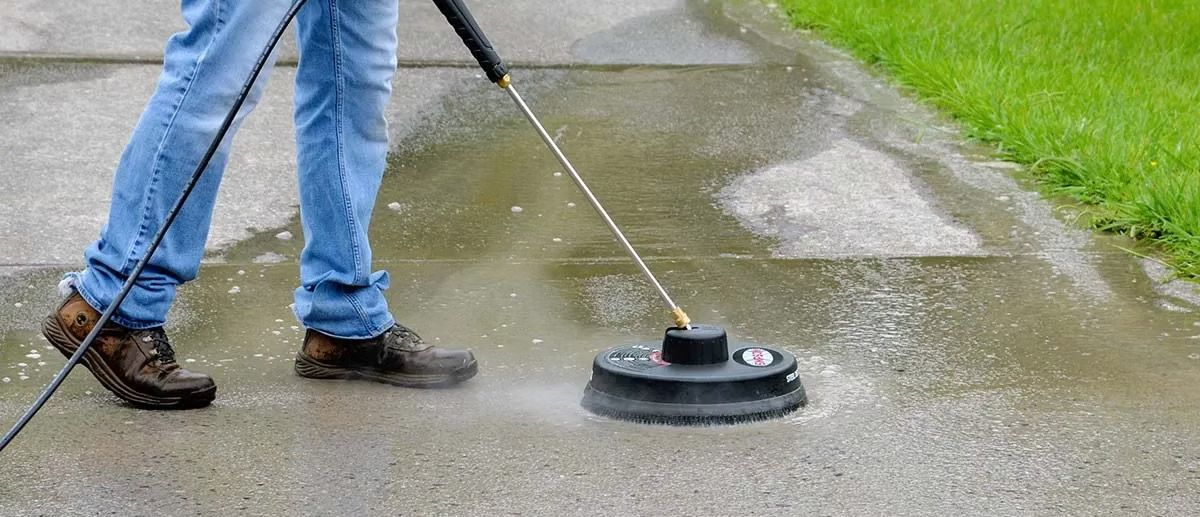 Person pressure washing a concrete walkway with water spraying.