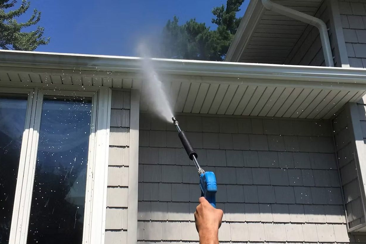 A person using a pressure washer to clean the siding of a house.