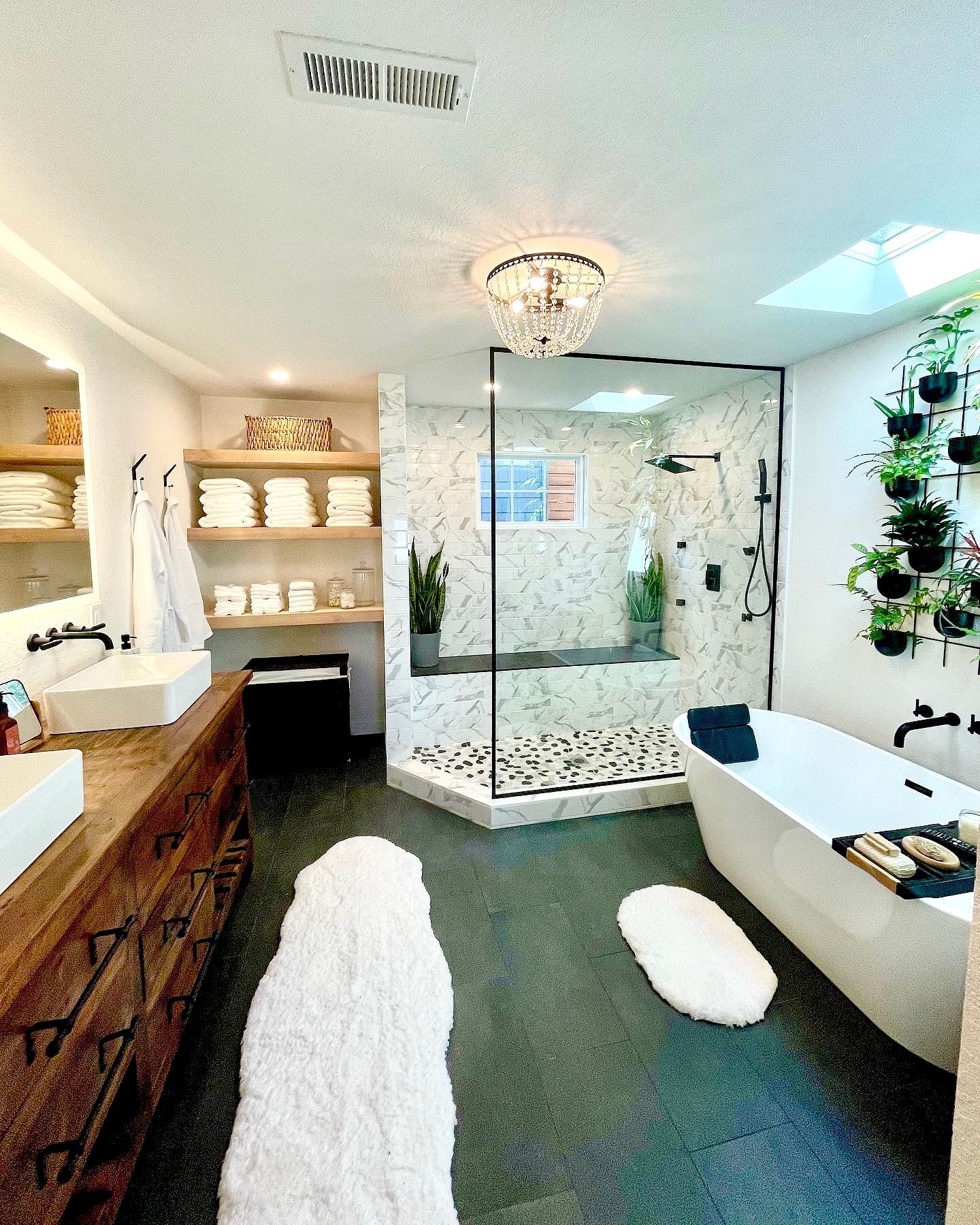 A modern bathroom with a glass shower, soaking tub, double vanity, and live plants.