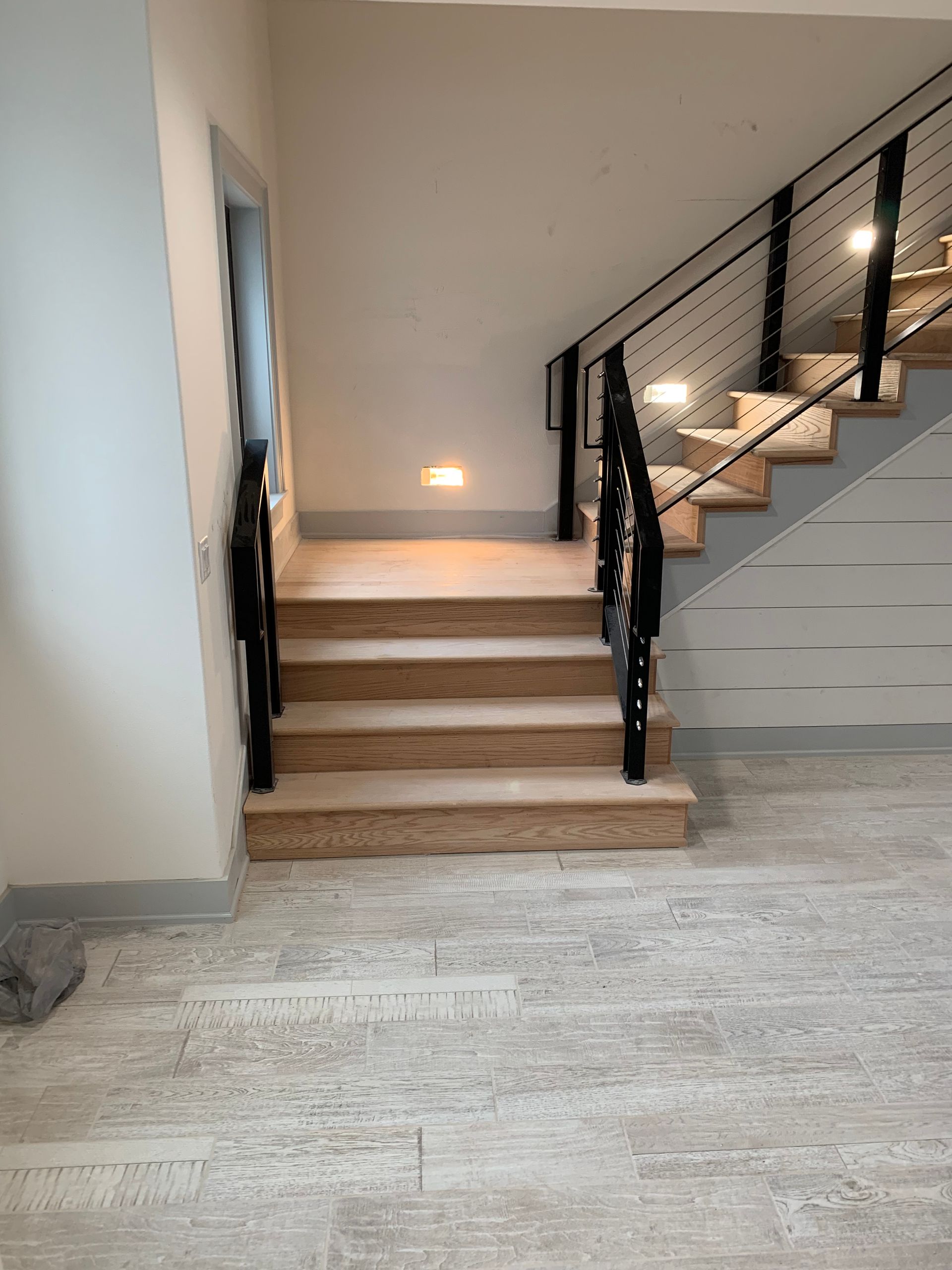 Staircase with wooden steps and black railing. Built-in lights illuminate the stairs and surrounding wall.