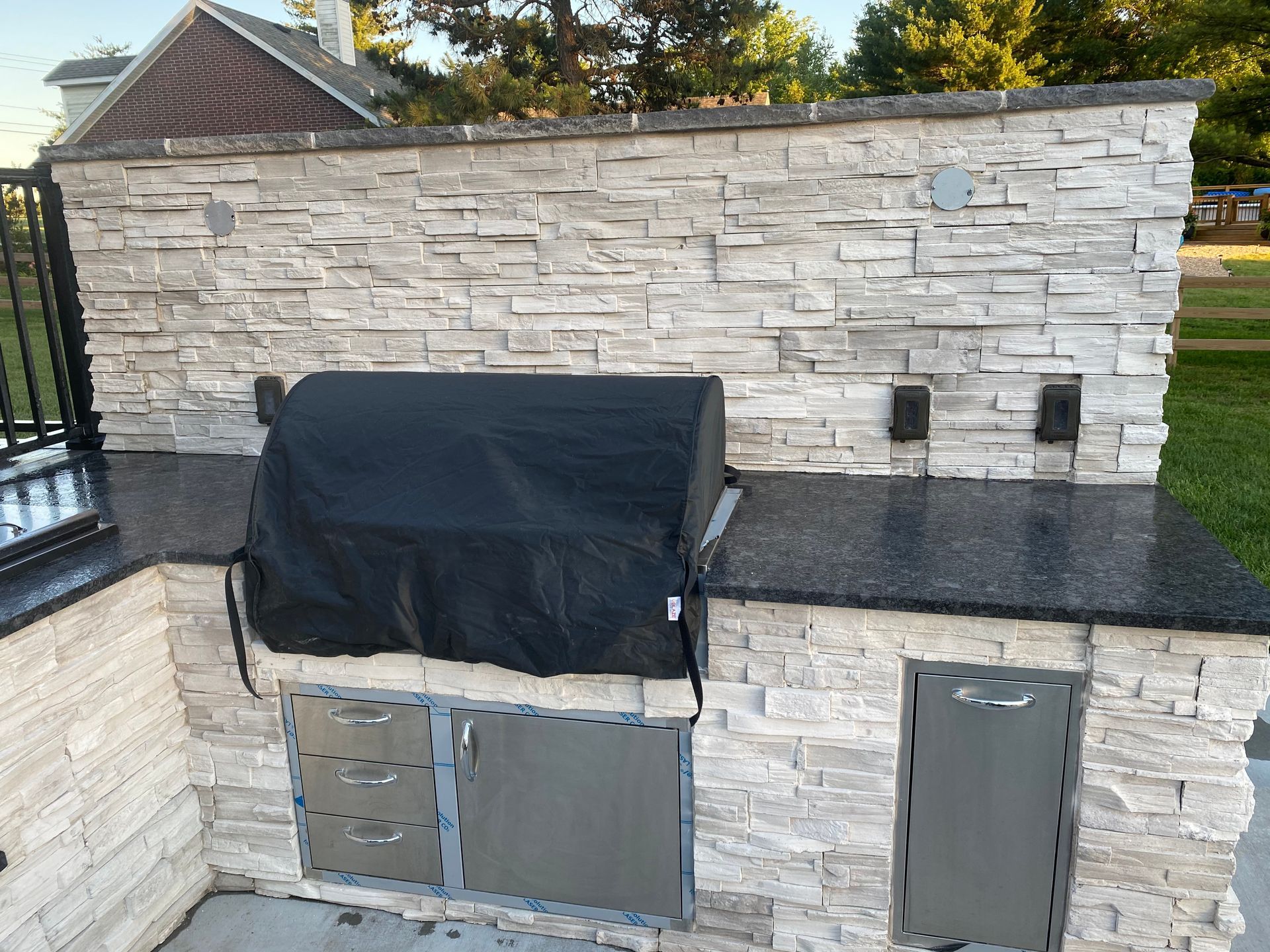 Outdoor kitchen with stone facade, black grill cover, and dark countertop.