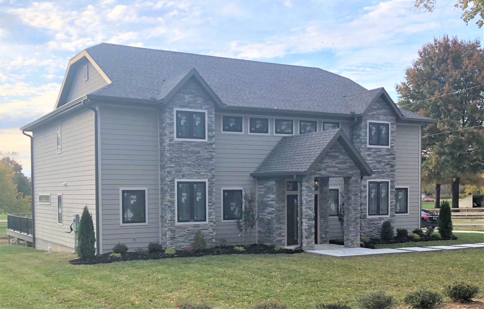 Two-story house with gray stone accents, light siding, and a dark roof on a grassy lot.