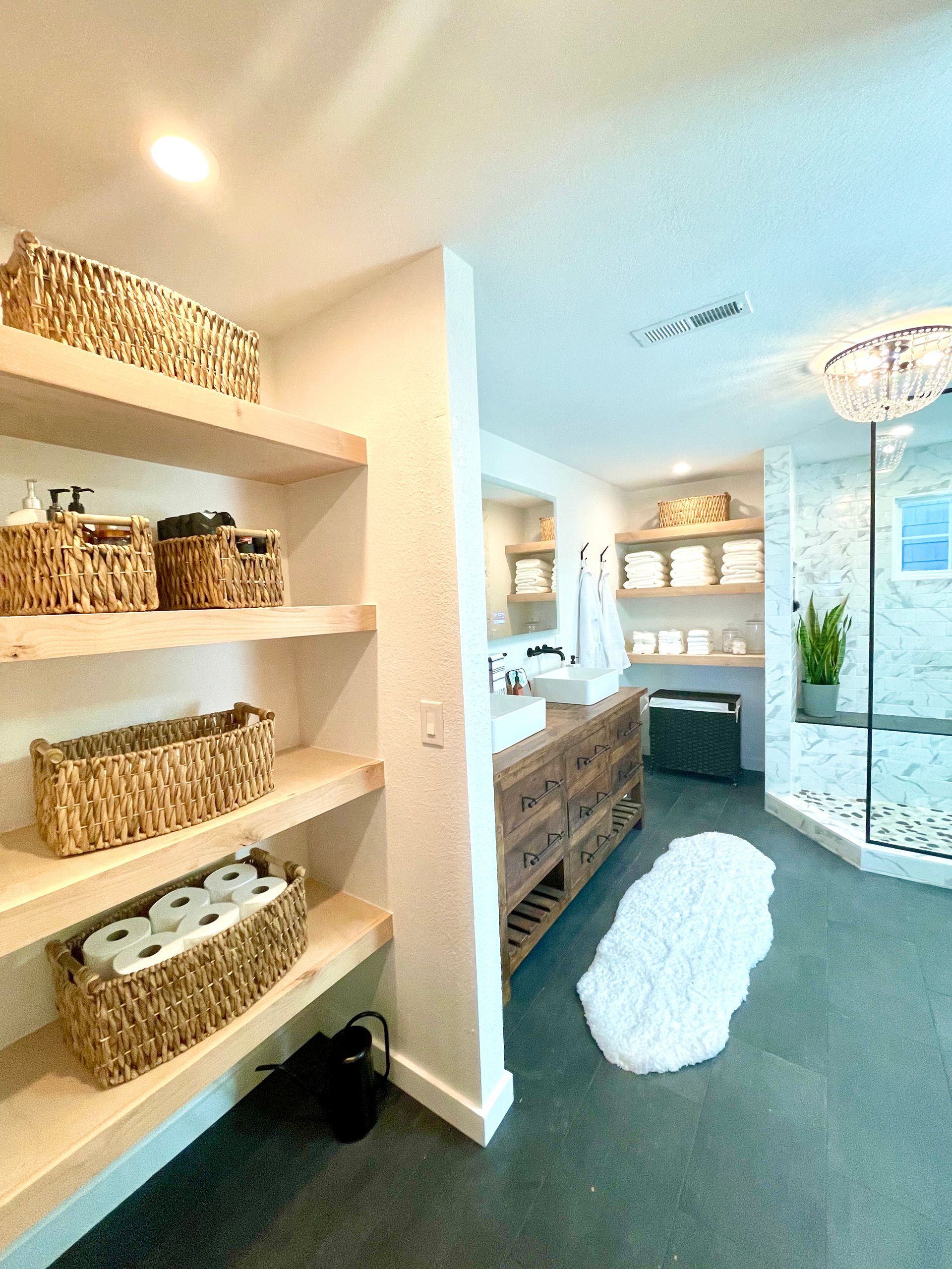 Bathroom with open shelves, baskets, a vanity, and a shower with a chandelier.