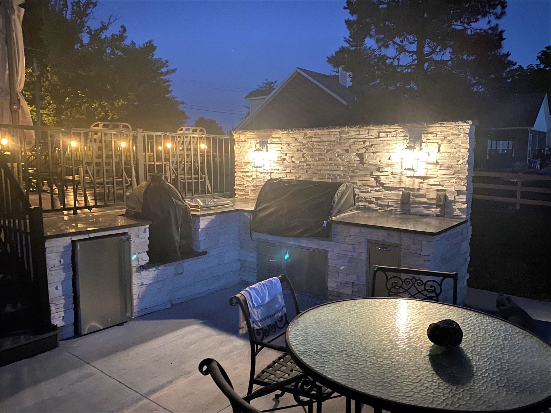 Outdoor kitchen at dusk with grill, seating, and stone accents.